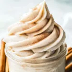 Swirled cinnamon cream cheese frosting piped into a glass jar with cinnamon sticks in the background