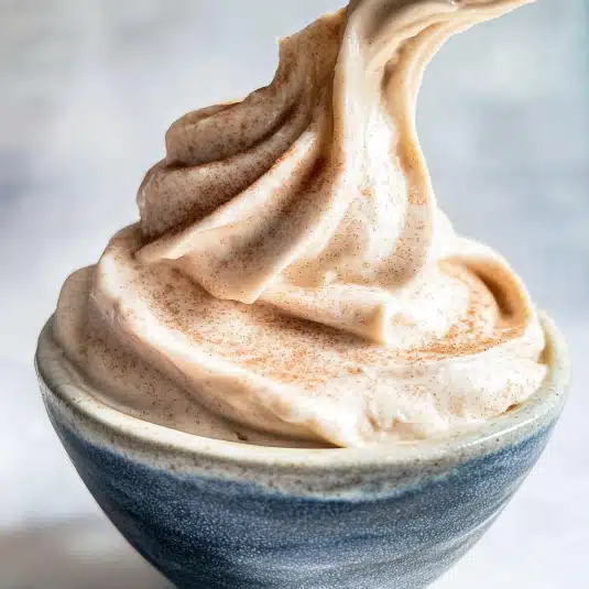 Smooth and fluffy cinnamon cream cheese frosting in a ceramic bowl, with a swirl and dusting of cinnamon