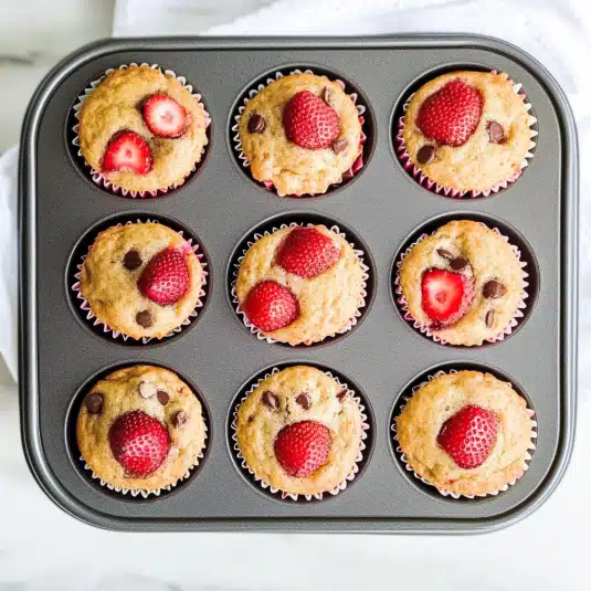 Freshly baked strawberry protein muffins with chocolate chips in a nonstick muffin tin lined with paper cups