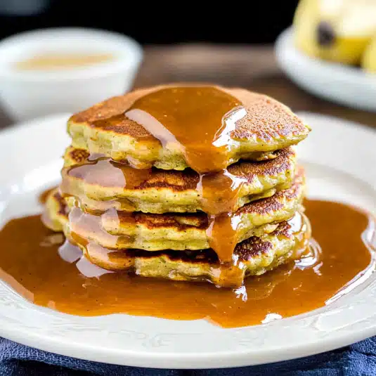 zucchini banana pancakes on a white plate, topped with syrup and a bite taken out.