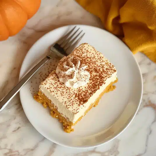 lice of pumpkin tres leches cake with whipped cream and cocoa dusting on a white plate with a fork
