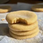 Soft and chewy brown butter sugar cookies stacked on parchment paper, with one cookie showing a bite taken out for texture.