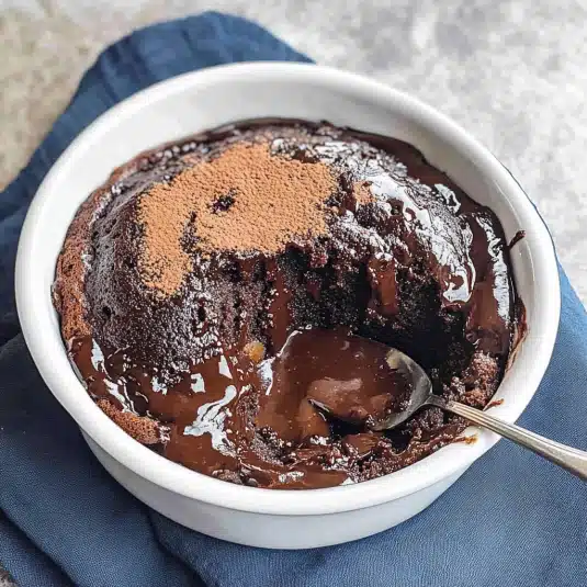 Rich and gooey chocolate pudding cake with a soft, fudgy sauce layer, served warm in a white ramekin with a spoon the perfect self-saucing dessert.
