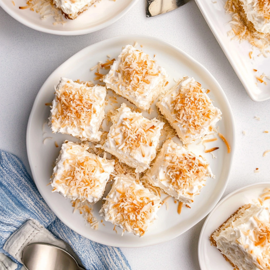 coconut poke cake topped with fluffy whipped topping and toasted coconut flakes in a white baking dish.