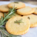Close-up of golden rosemary shortbread cookies topped with fresh rosemary sprigs, arranged on parchment paper