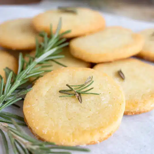 Close-up of golden rosemary shortbread cookies topped with fresh rosemary sprigs, arranged on parchment paper