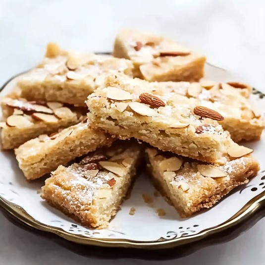 Buttery almond shortbread bars topped with sliced almonds and powdered sugar, baked until golden and served on a white plate.