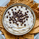 Bowl of creamy cannoli dip topped with chocolate chips, served with waffle cookie pieces around the dish.
