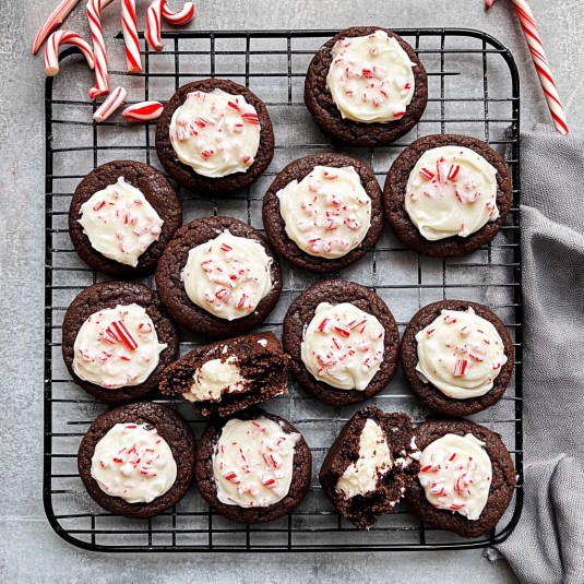 Cooling rack filled with chocolate peppermint cookies topped with white peppermint frosting and crushed candy canes.