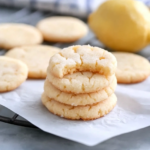 Soft and chewy lemon sugar cookies stacked on parchment paper with fresh lemon in the background