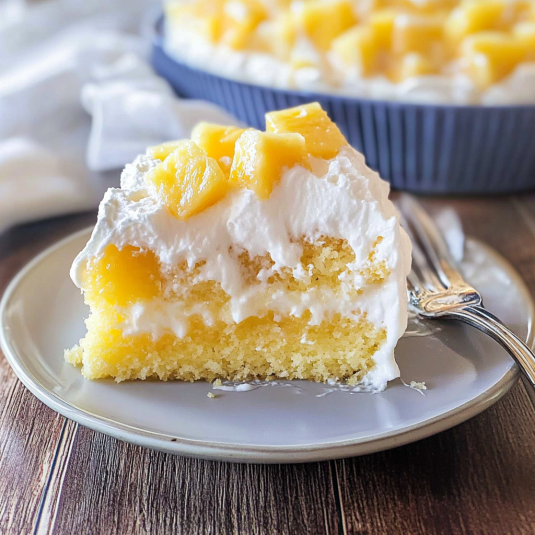 Pineapple poke cake slice with whipped cream topping and pineapple chunks on a plate