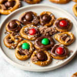 Rolo pretzels topped with melted chocolate, candy pieces, and chocolate candies on a serving plate